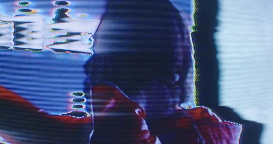 Woman stands looking around as digital screen and lights flash all around her before reaching out to touch wall