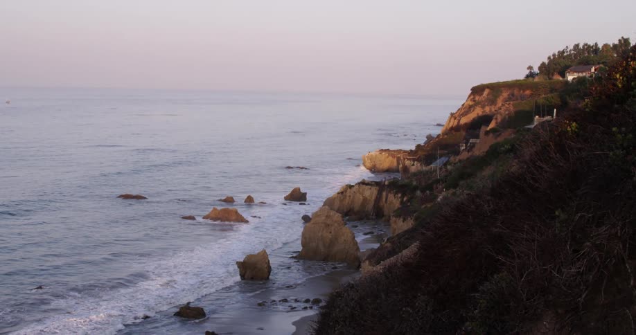 Waves crash against rocks near the shore at sunset