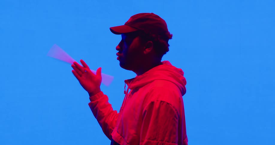 A man with a hat twirling a drumstick in a room with a screen in the background