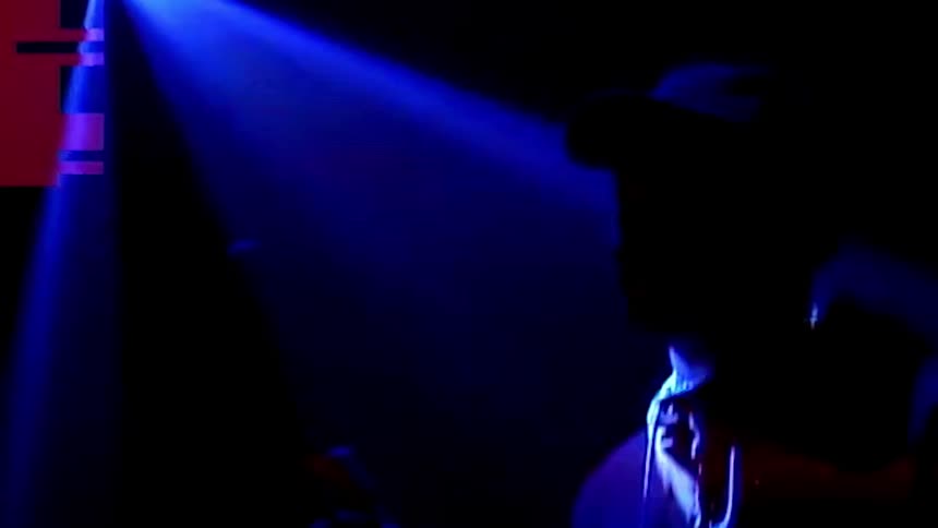 A man with a hat twirling a drumstick in a room with laser lights
