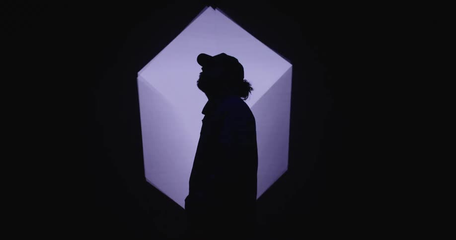 A man is wearing a hat and standing by a digital display