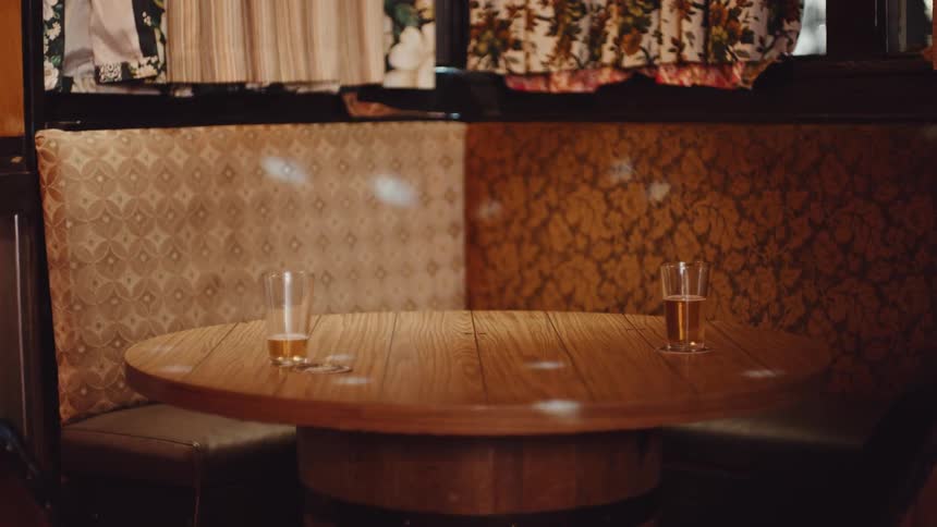 Two beer glasses sit on a round table as lights dance across it and the bench seats