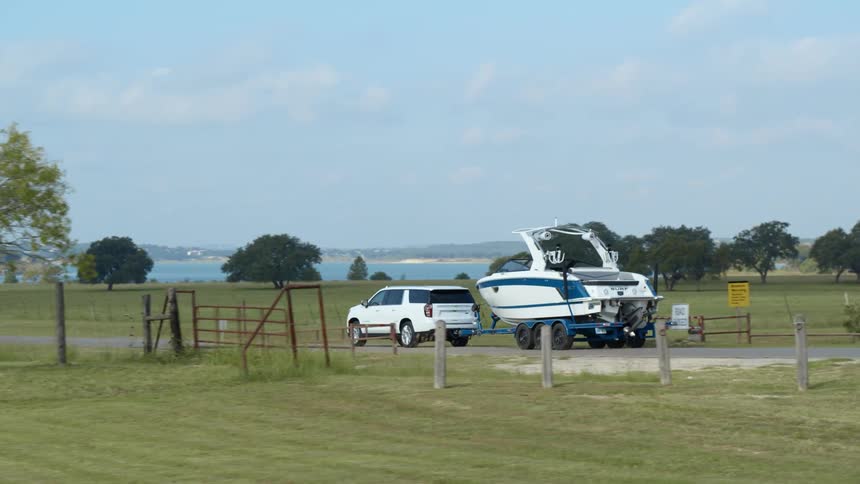 An suv car is towing a boat and driving on a long straight road