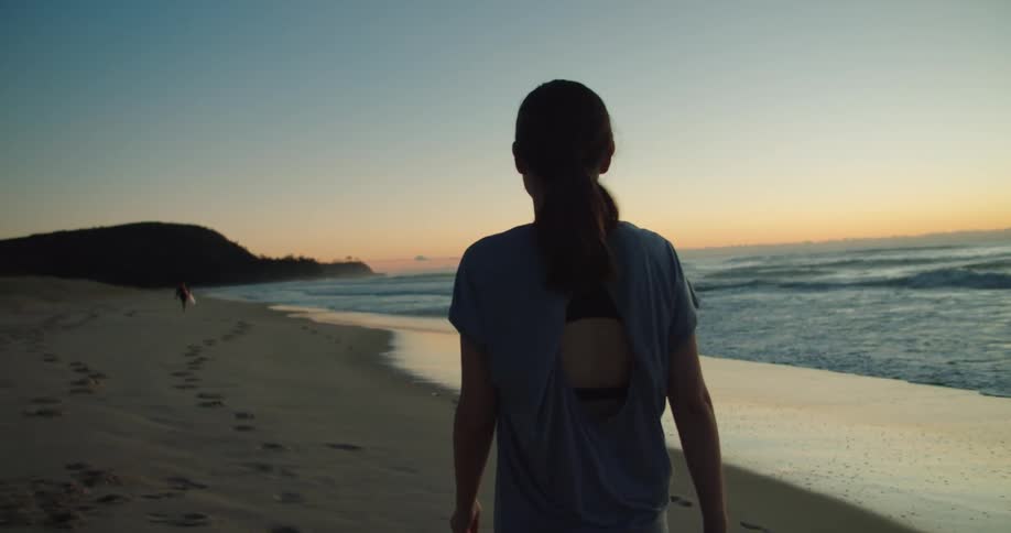 A woman is standing outdoors at the beach at dusk