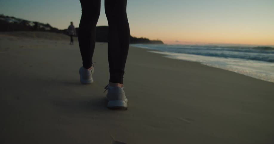 A person walks on the sandy beach beside the ocean water with the sun low on the horizon