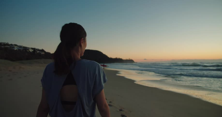 A woman walking alone on a sandy beach at sunset