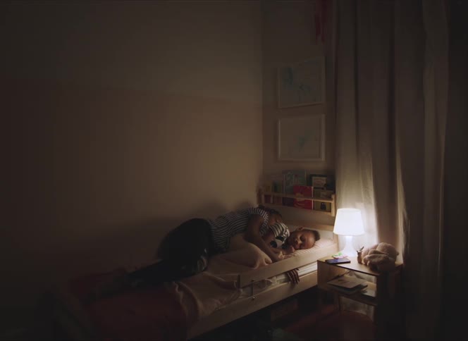 A woman resting down a smart phone and laying in a bed next to a girl in a bedroom