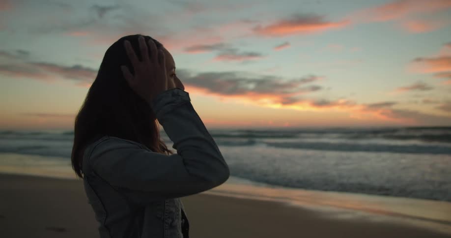 Woman standing and watching the sea on the beach is silhouetted against the red sky