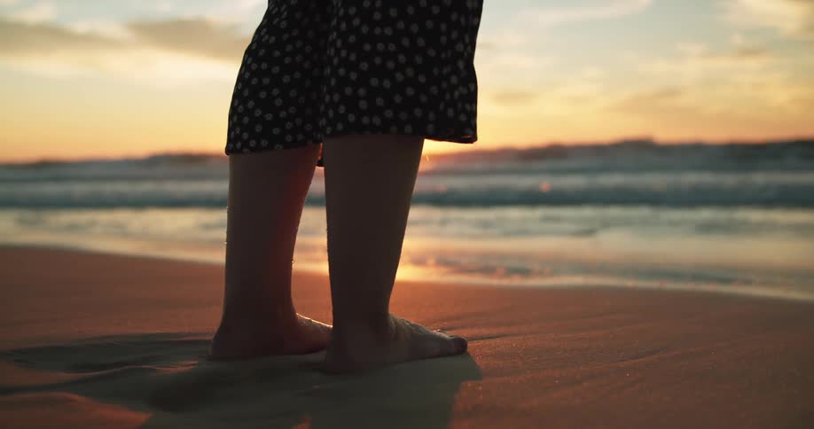 Woman wearing a dress standing on the sand next to the ocean at sunset