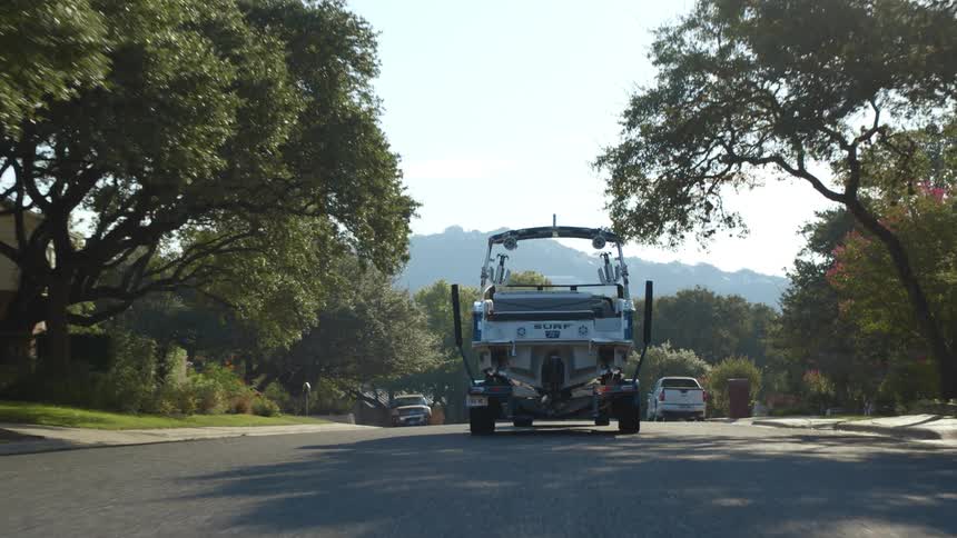 A sport utility vehicle tows a boat down a windy residential street