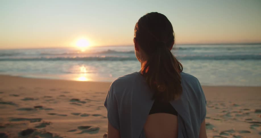 A young woman sits on the beach and watches the sunset