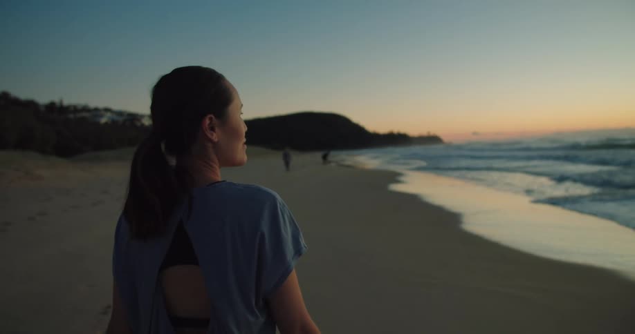 A woman is walking on the beach at dusk