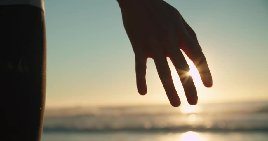 Sun shines from over ocean silhouetting persons hand