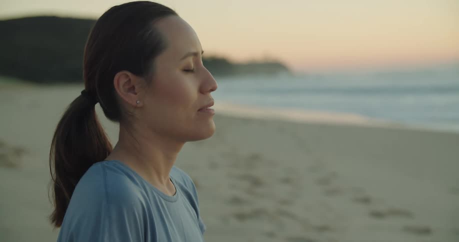 A woman sits cross legged and meditates on the beach