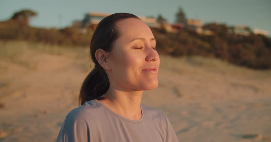 A woman is sitting at the beach while the sun is setting