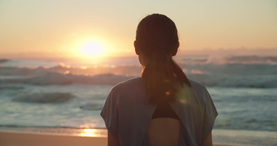 Woman looking at the sunset on the sand next to the ocean