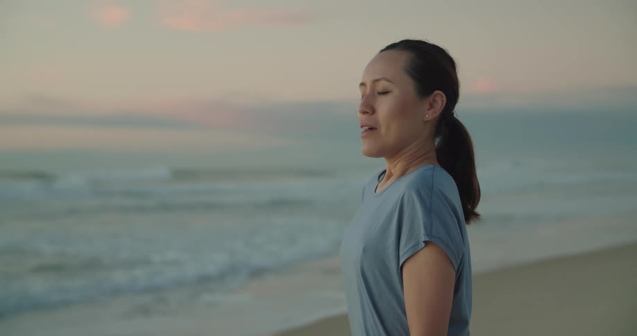 A woman stands on the sandy beach by herself and takes a deep relaxing breath