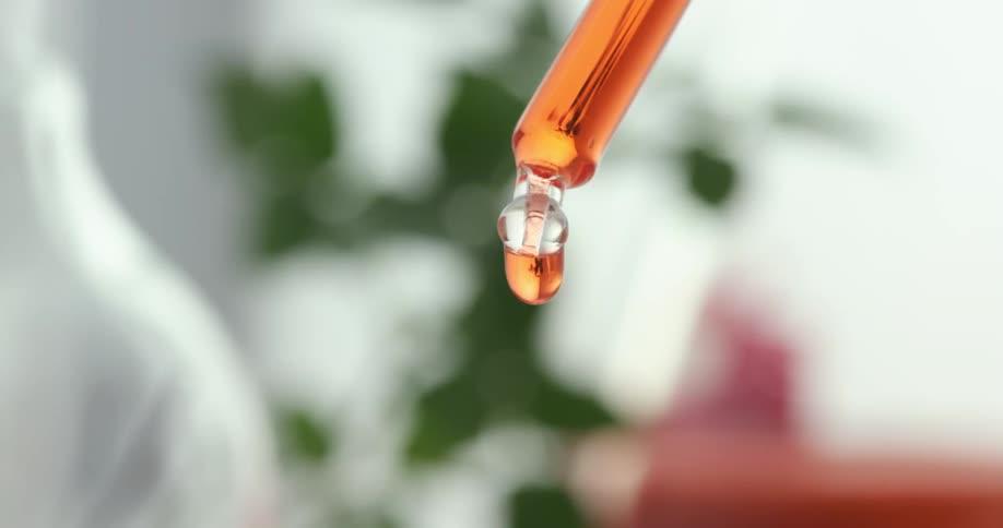 A glass vial is dripping orange liquid