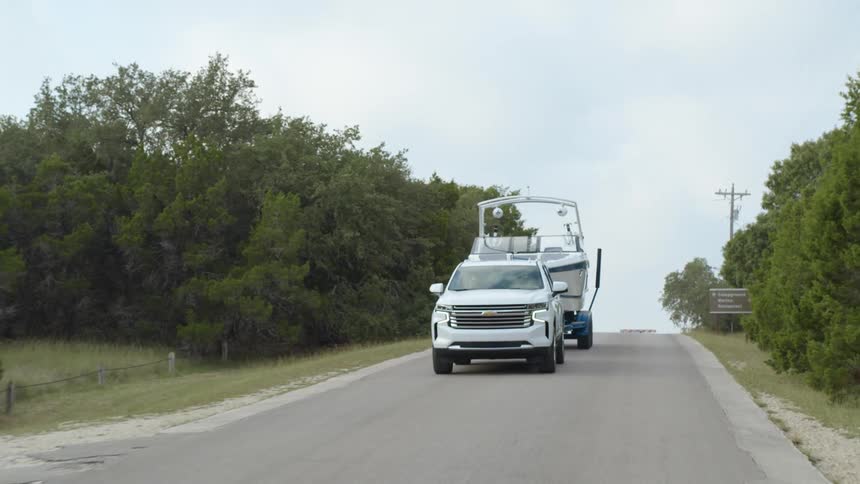 White vehicle tows a boat down the road that is lined with trees