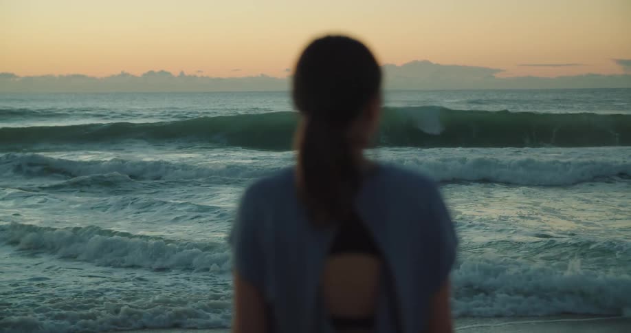 Woman standing in front of the ocean looking at the sunset