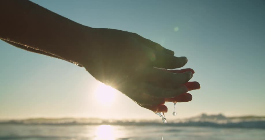 Woman washing her hands on the beach near the ocean at sunset