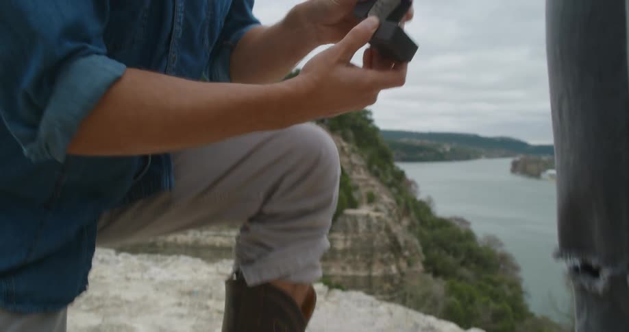 A man removes an engagement ring from his cowboy boot and proposes to a woman while they are on a cliff