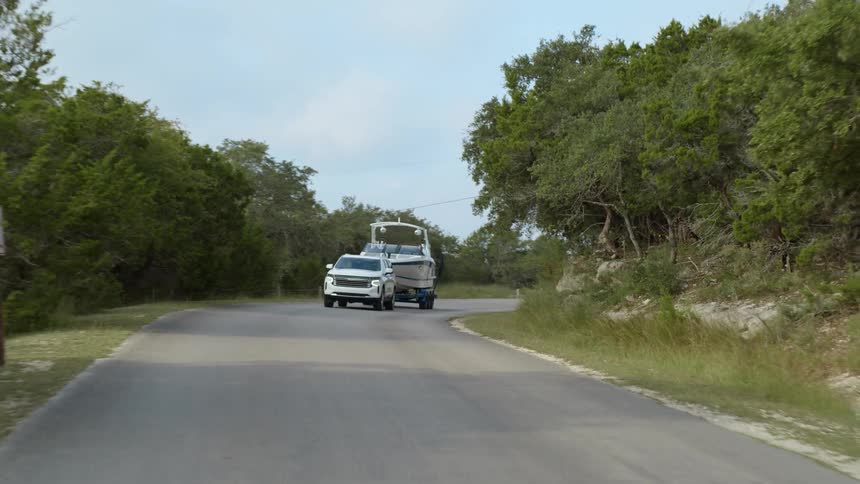 A vehicle towing a boat on a road with the sky and clouds in the background