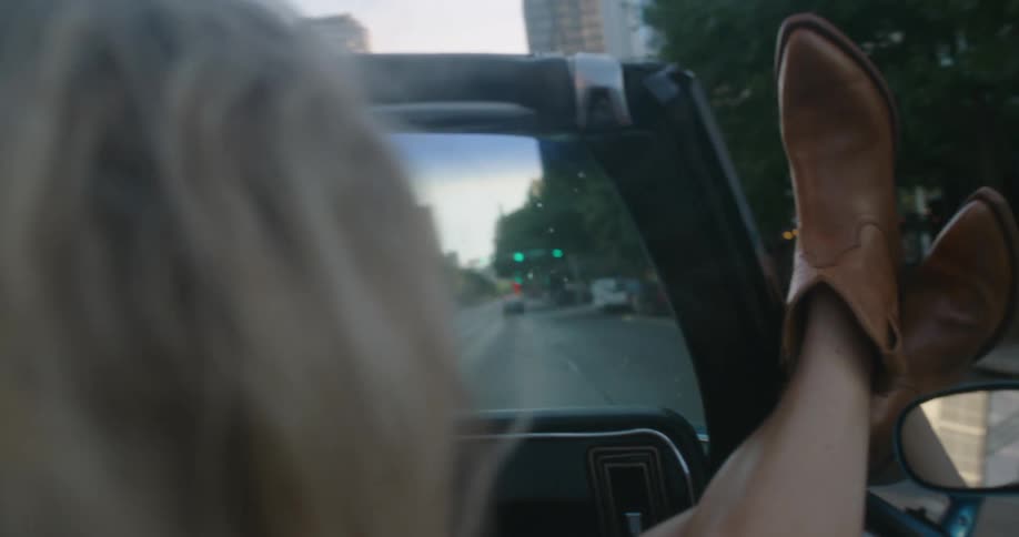 Woman on the passenger seat of a convertible with her feets out the window