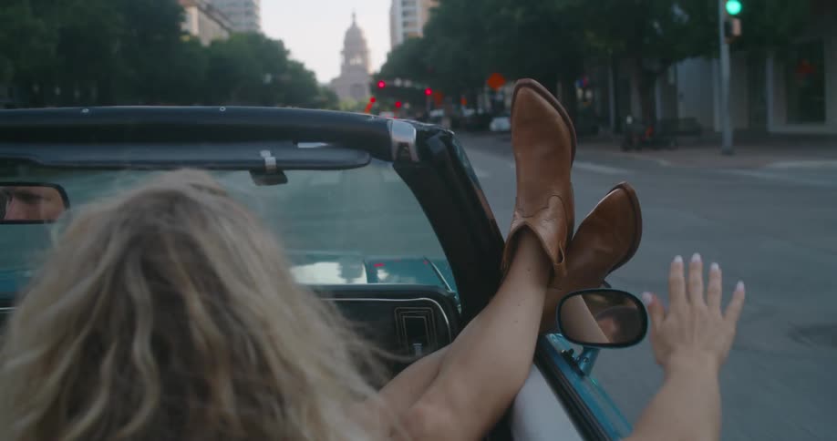 Woman with her feet out the window of a convertible driving in the city
