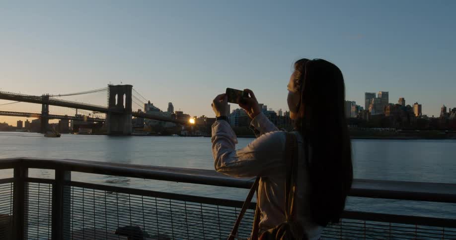 A woman is walking and taking pictures of the skyline at dusk