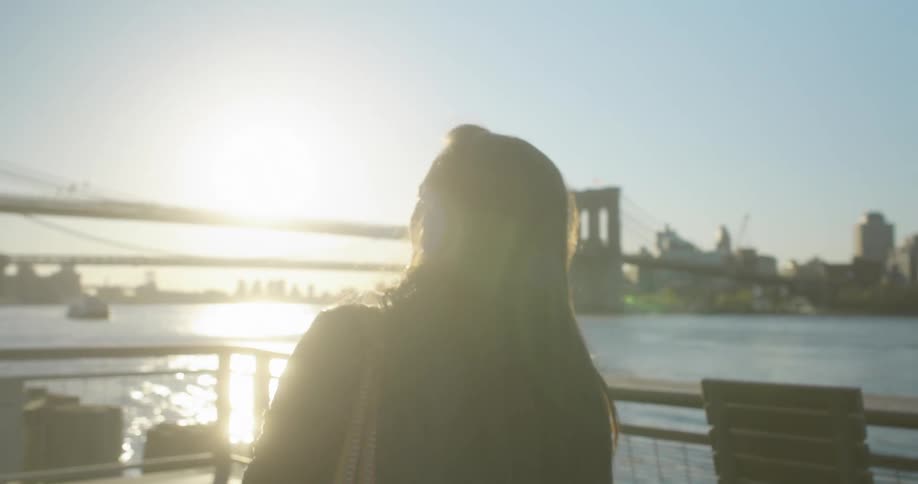 A woman walks to the end of a pier looking at the river city and bridge