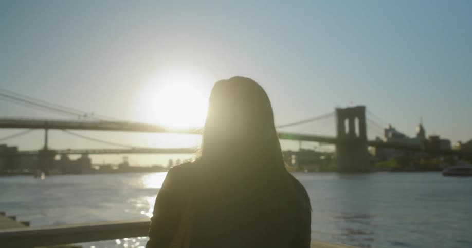 Woman stops at the boardwalk to look at the sunset over the river in the city