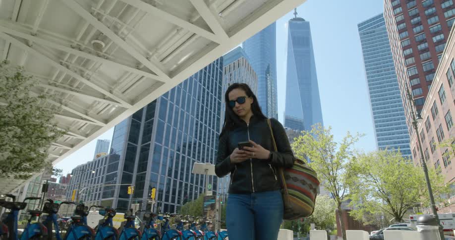 Woman wearing sunglasses looks at her cellphone as she walks past a row of bicycles in the city