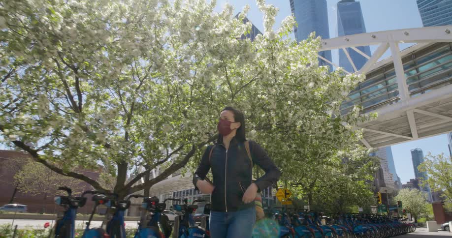 A woman zips up her jacket while walking down a city sidewalk as vehicles pass by