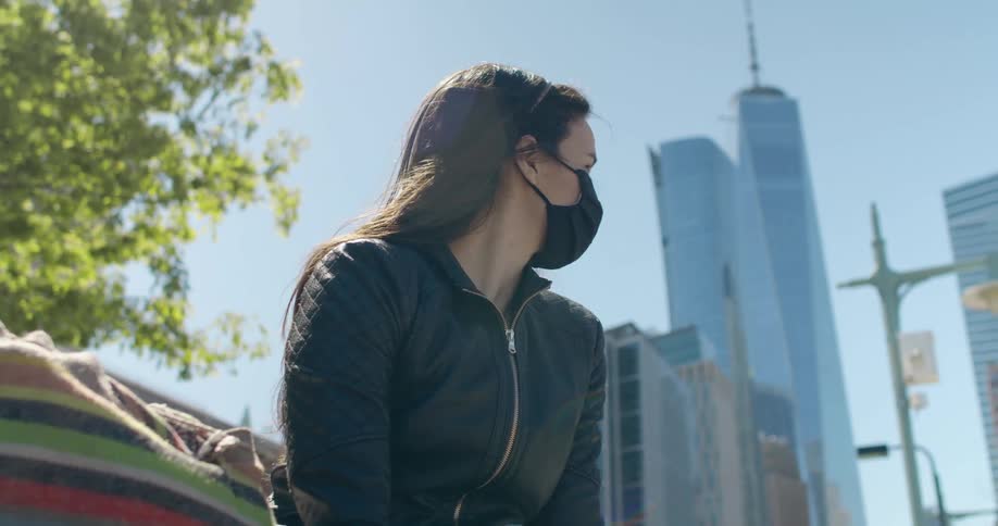 Woman wearing a black face mask sitting on a bench in the city