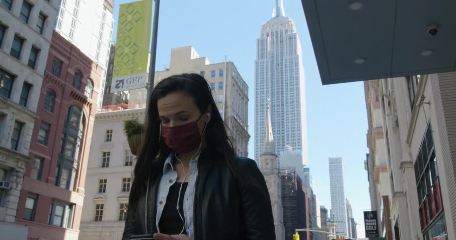 A woman wearing a mask is walking in city while looking at her phone