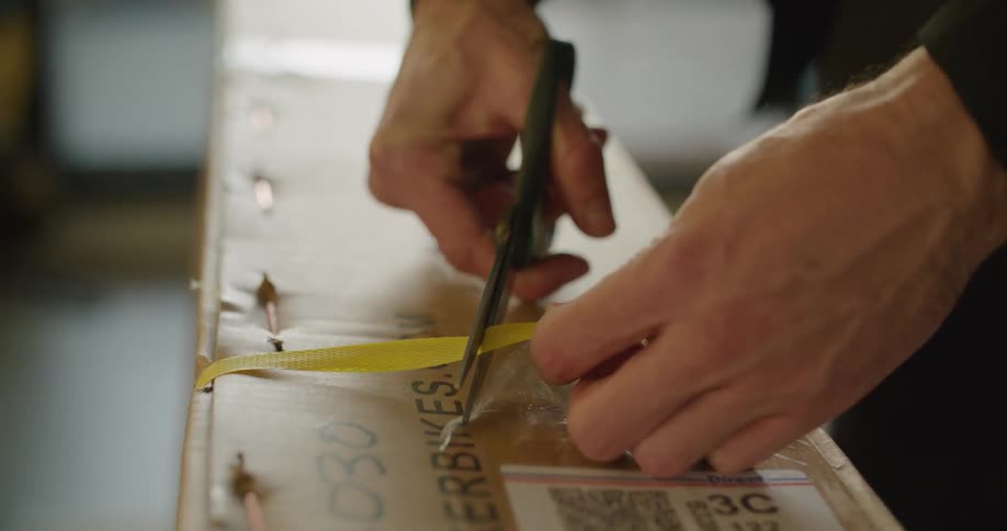 A person cutting a strap off of a cardboard box