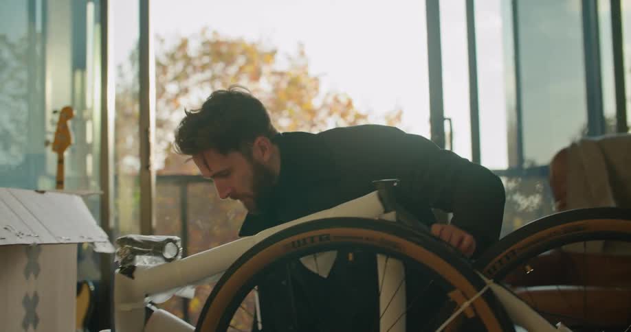 A man is putting a bike together while sitting indoors