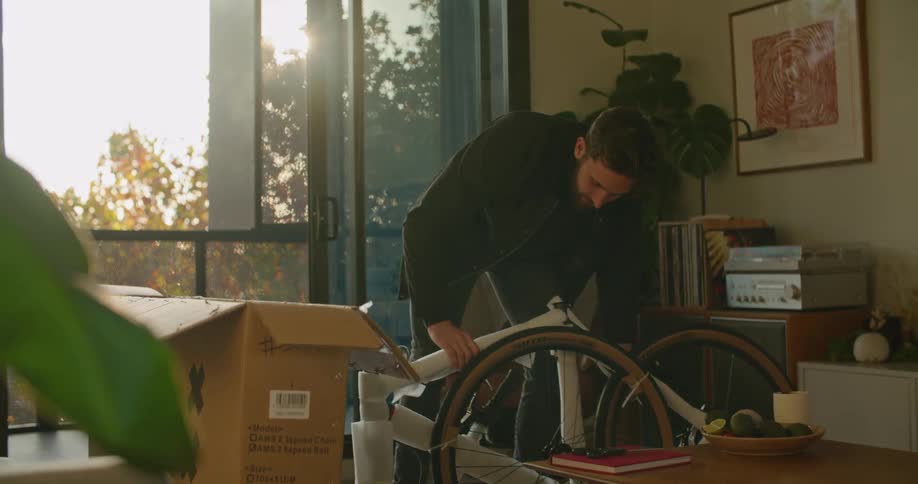 A man in a room taking an unassembled bicycle from a box with a wall in the background