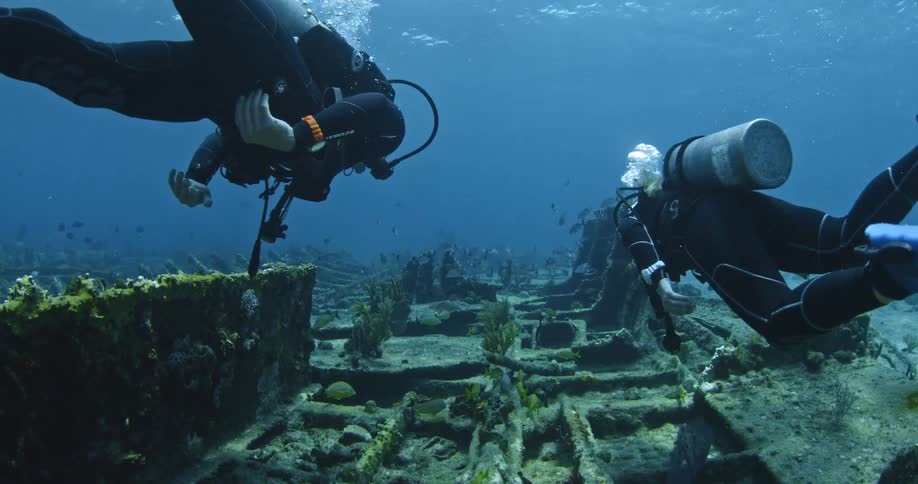 Two divers swim along the wreckage of a boat