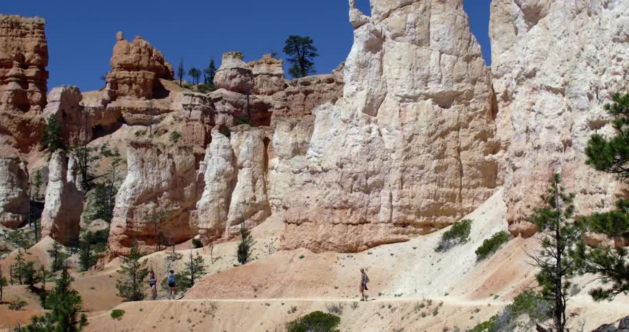 Three people are walking below the base of cool rock formations