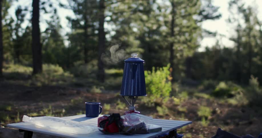 A coffee pot steams on a small camp stove on a sunny day