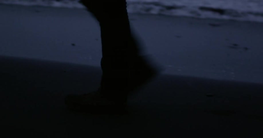 A person's legs and feet as they walk on a beach at dusk