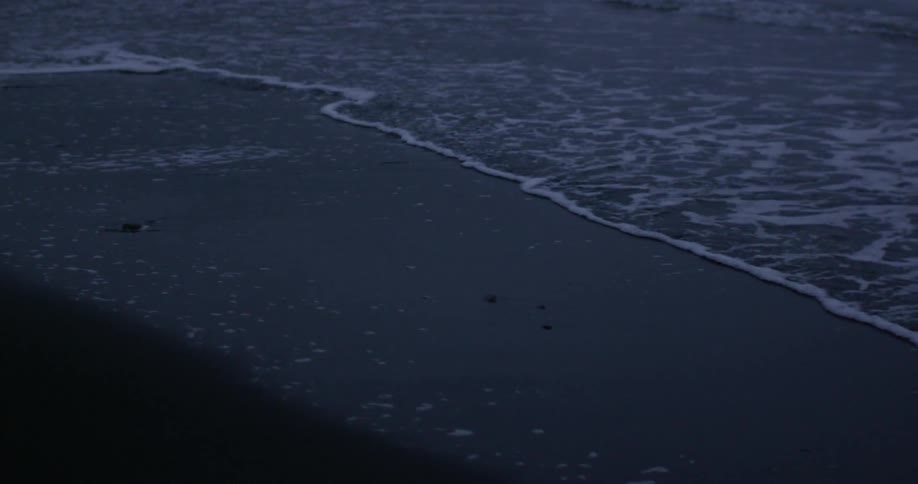 Ocean water gently rolling onto a beach after sunset
