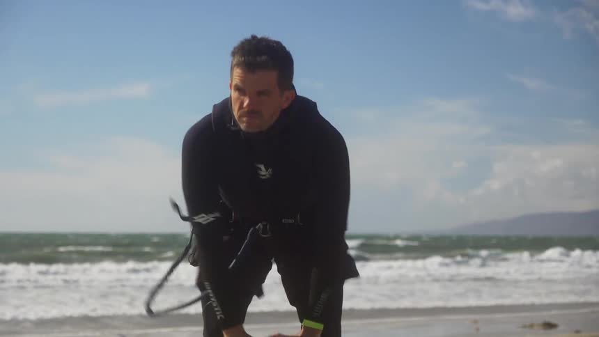 A man pumping up a kiteboarding kite on the beach