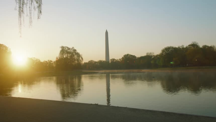 The washington monument and the lincoln memorial reflecting pool with a bright sun on the horizon