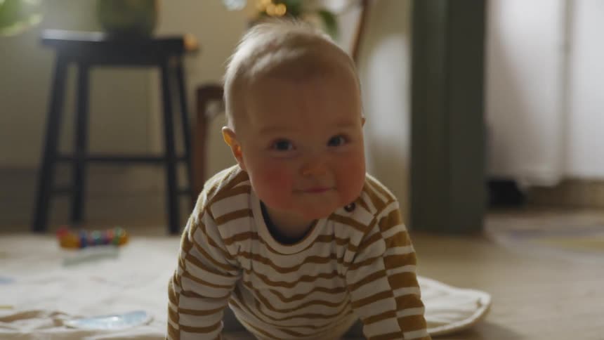 A young baby crawls across a mat and smiles as it makes its way to the camera