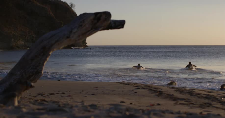 The silhouette of two men running into the ocean and jumping on their surfboards to paddle out