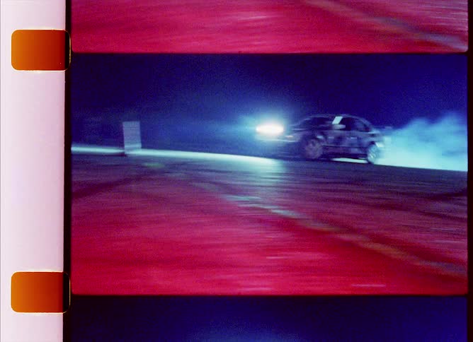 Sports car leaves a trail of smoke behind while drifting on a race track at night