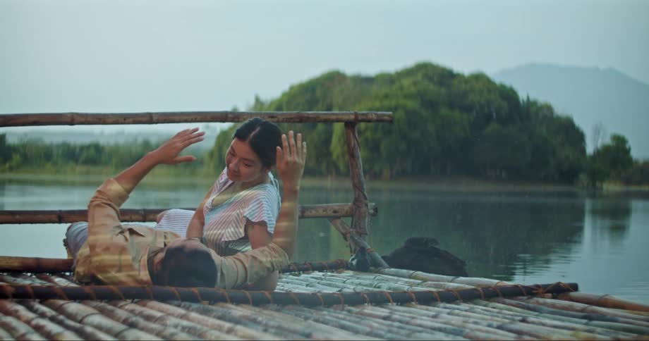 A couple are lying on bamboo structure lakeside as they talk